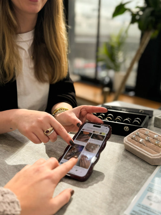 A customer and jeweler browsing engagement ring styles on a phone at the Ethan Lord Jewelers showroom in Chicago. A tray of diamond rings is displayed on the table.