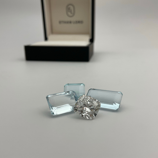 Loose aquamarine and cushion cut diamond gemstones displayed in front of Ethan Lord Jeweler ring box