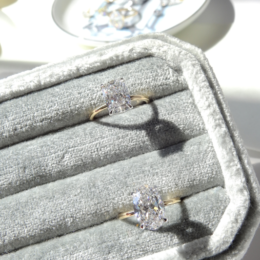 Two solitaire diamond engagement rings featuring radiant and oval-cut diamonds in prong settings with yellow gold bands, displayed in a light gray velvet jewelry box at Ethan Lord Jewelers.