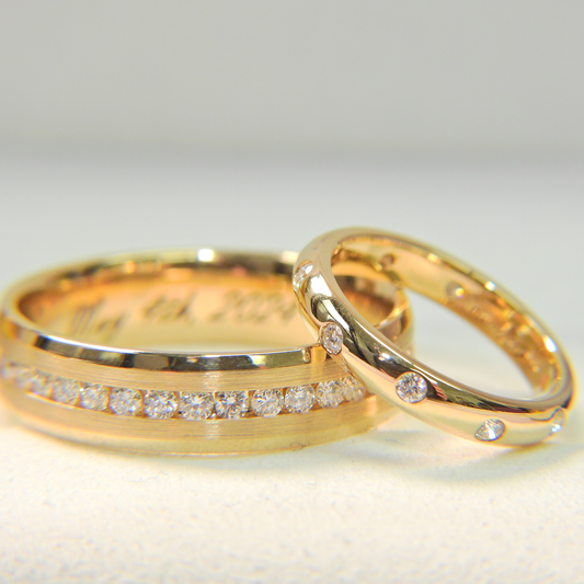 Close-up of matching yellow-gold wedding bands with round-cut diamond accents, one featuring a channel-set row of diamonds and the other with scattered diamond settings.