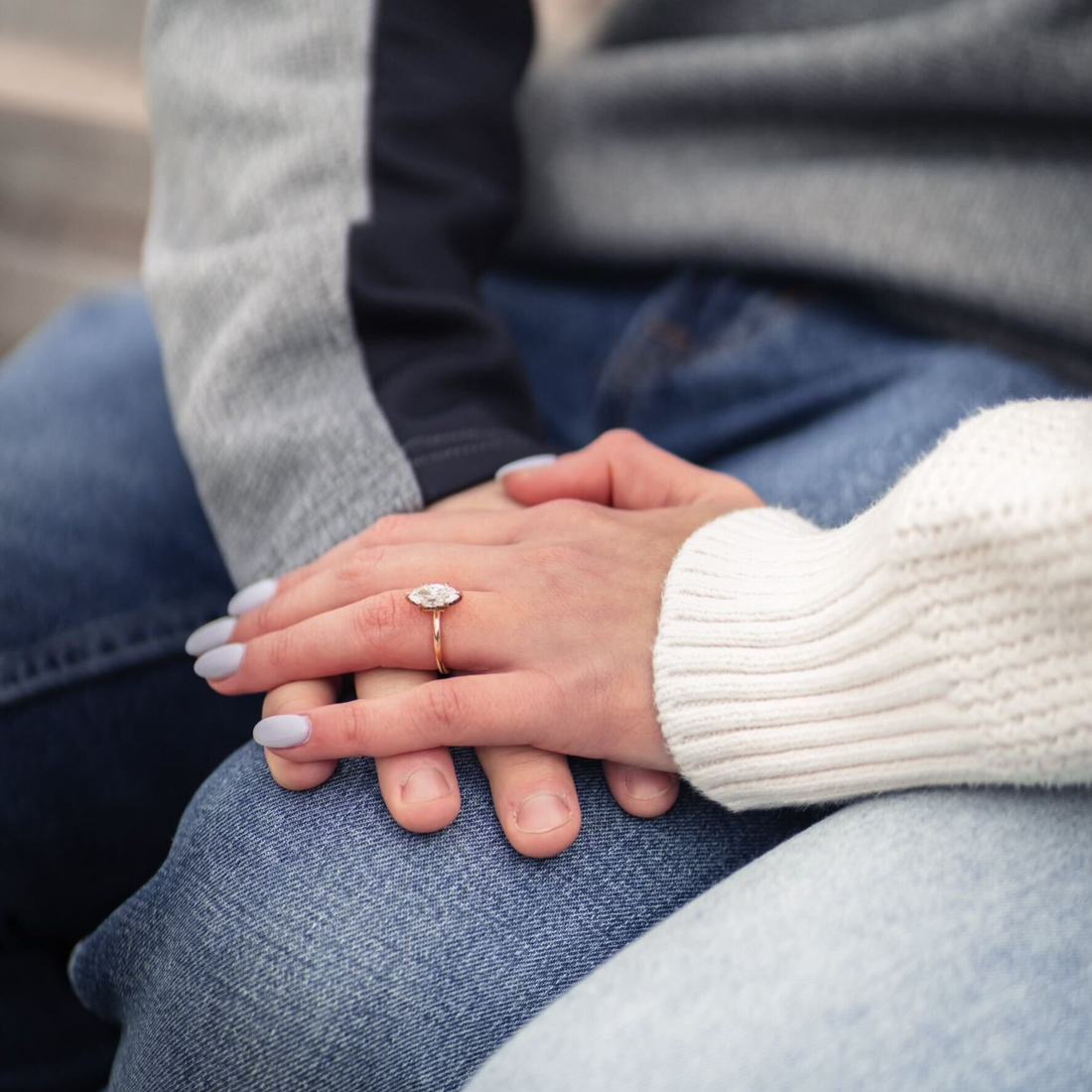 Close-up of a couple holding hands, featuring a marquise-cut diamond engagement ring on a yellow-gold band.