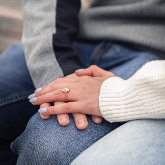 Close-up of a couple holding hands, featuring a marquise-cut diamond engagement ring on a yellow-gold band.